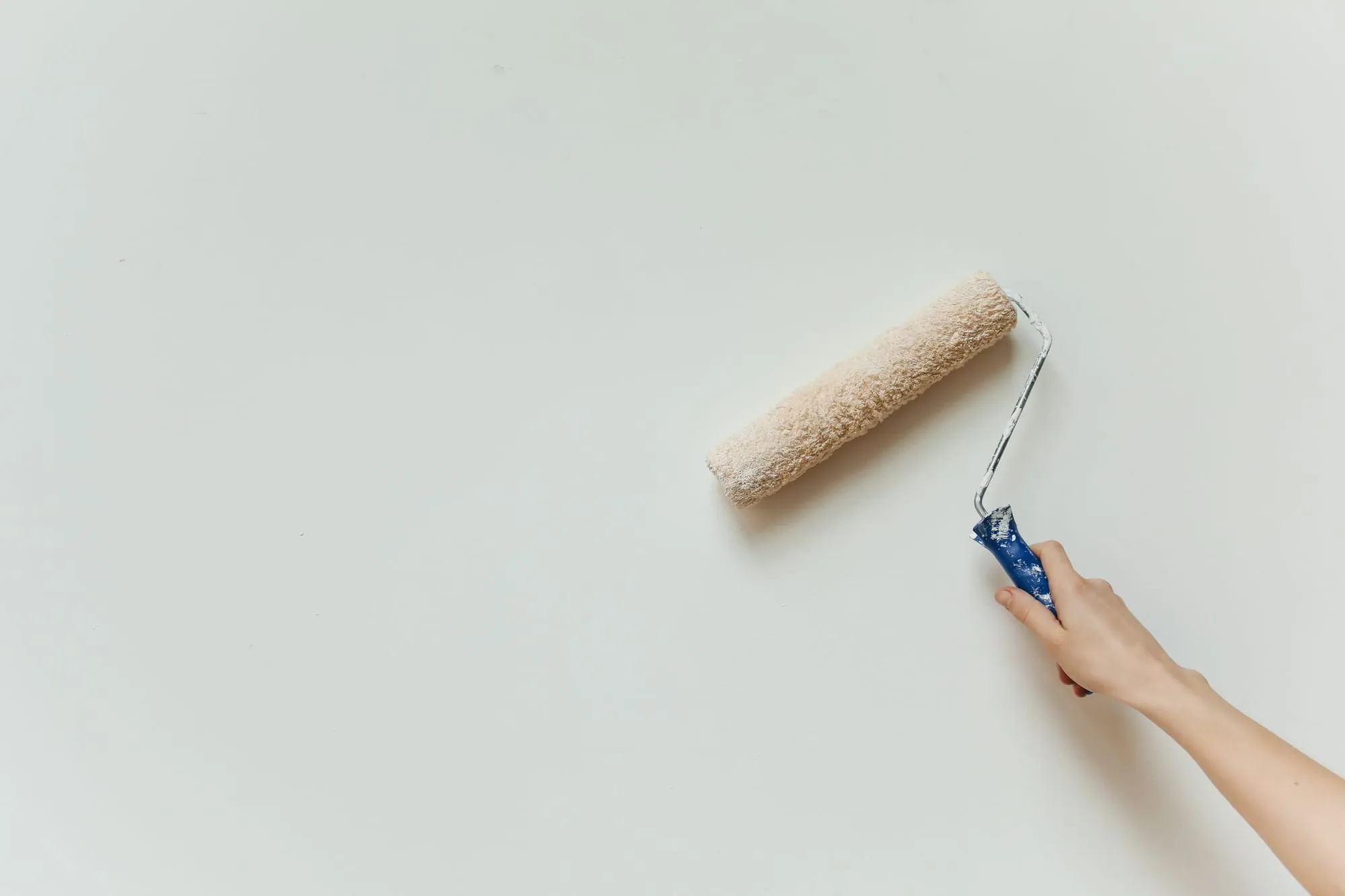 Hand streicht mit der Farbrolle eine helle Wand